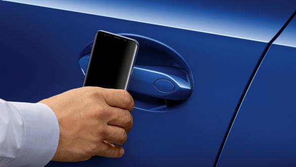 BMW 3. sērijas Sedan, digitālā atslēga BMW 3. sērijas Sedan vadītāja durvju tuvplāns ar Samsung mobilo tālruni, ko tur durvju roktura priekšā.