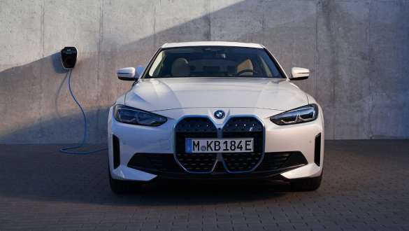 Priekšpuses skats ar BMW Wallbox BMW i4 eDrive40, G26, 2021 BMW i4 eDrive40, G26, 2021, Mineral White krāsa, priekšpuses skats uz ēkas sienas fona ar BMW Wallbox uzlādes staciju