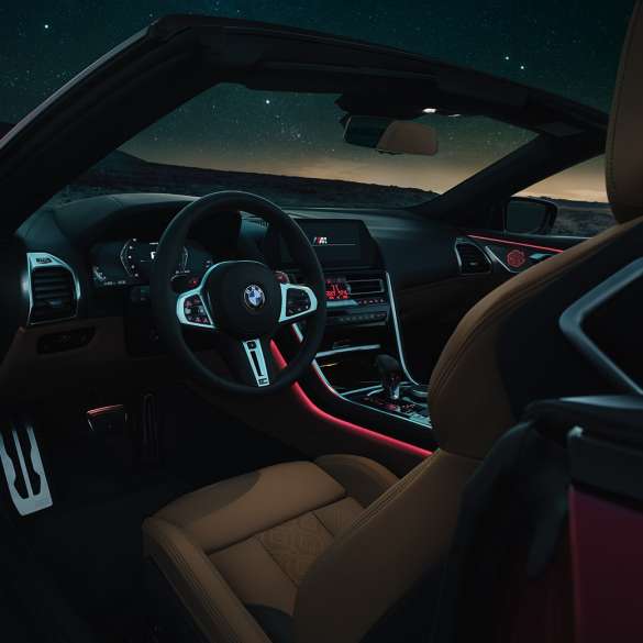 BMW M8 Competition Cabrio, kokpits. BMW M8 Competition Cabrio, kokpits naktī ar M ādas stūri un sarkanu fona apgaismojumu.