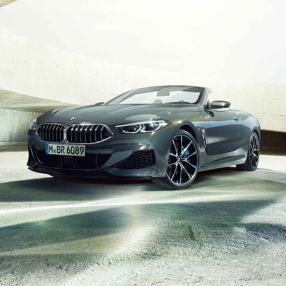 BMW M850i xDrive Cabrio, trīs ceturtdaļu skats no priekšpuses. BMW M850i xDrive Competition Cabrio metāliskā Dravit Grey krāsā ar nolaistu mīkstā seguma jumtu, trīs ceturtdaļu skats no priekšpuses, stāvošs automobilis betona ēkā.
