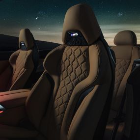Merino ādas M sporta sēdekļi. BMW M8 Competition Cabrio ar nolaistu mīkstā seguma jumtu zem zvaigžņotām debesīm, salons ar M sporta sēdekļiem ar Merino ādu un sarkanu fona apgaismojumu.