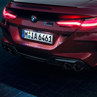 BMW M8 Competition Cabrio, aizmugures tuvplāns. BMW M8 Competition Cabrio metāliskā Motegi Red krāsā, aizmugures tuvplāns ar LED aizmugures lukturiem un M8 Competiton emblēmu.