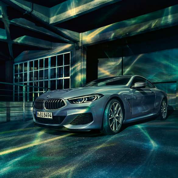 BMW M850i xDrive Coupé, trīs ceturtdaļu skats no priekšpuses. BMW M850i xDrive metāliskā Barcelona Blue krāsā, trīs ceturtdaļu skats uz novietotu automobili no priekšpuses uz ēkas fona.