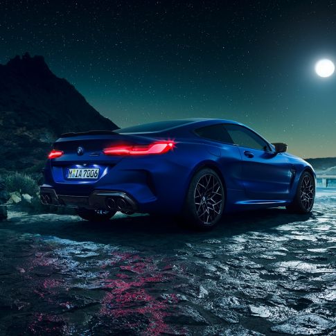 BMW M8 M Competition Coupé, trīs ceturtdaļu skats no aizmugures. BMW M8 Competition Coupé metāliskā Marina Bay Blue krāsā ar iedegtiem LED aizmugurējiem lukturiem, trīs ceturtdaļu skatā no aizmugures ar pilnmēnesi.
