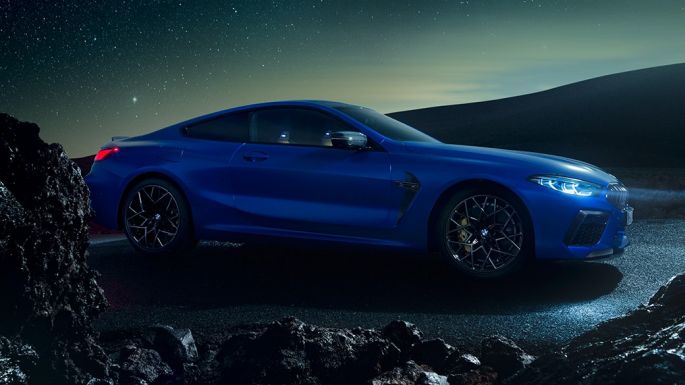 BMW M8 M Competition Coupé, trīs ceturtdaļu skats no sāniem. BMW M8 Competition Coupé metāliskā Marina Bay Blue krāsā, trīs ceturtdaļu skatā no priekšpuses uz stāvošu automobili naktī.
