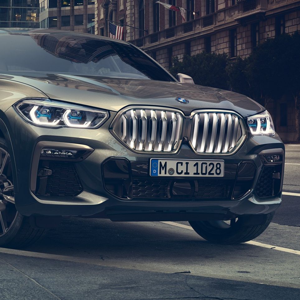 Novietots BMW X6 M50i BMW X6 M50i trīs ceturtdaļu skats uz novietotu automobili no priekšpuses uz pilsētas fona