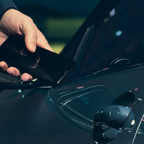 Digitālā atslēga Digitālā atslēga: Vīrietis automobiļa ārpusē pie tā durvīm tur viedtālruni