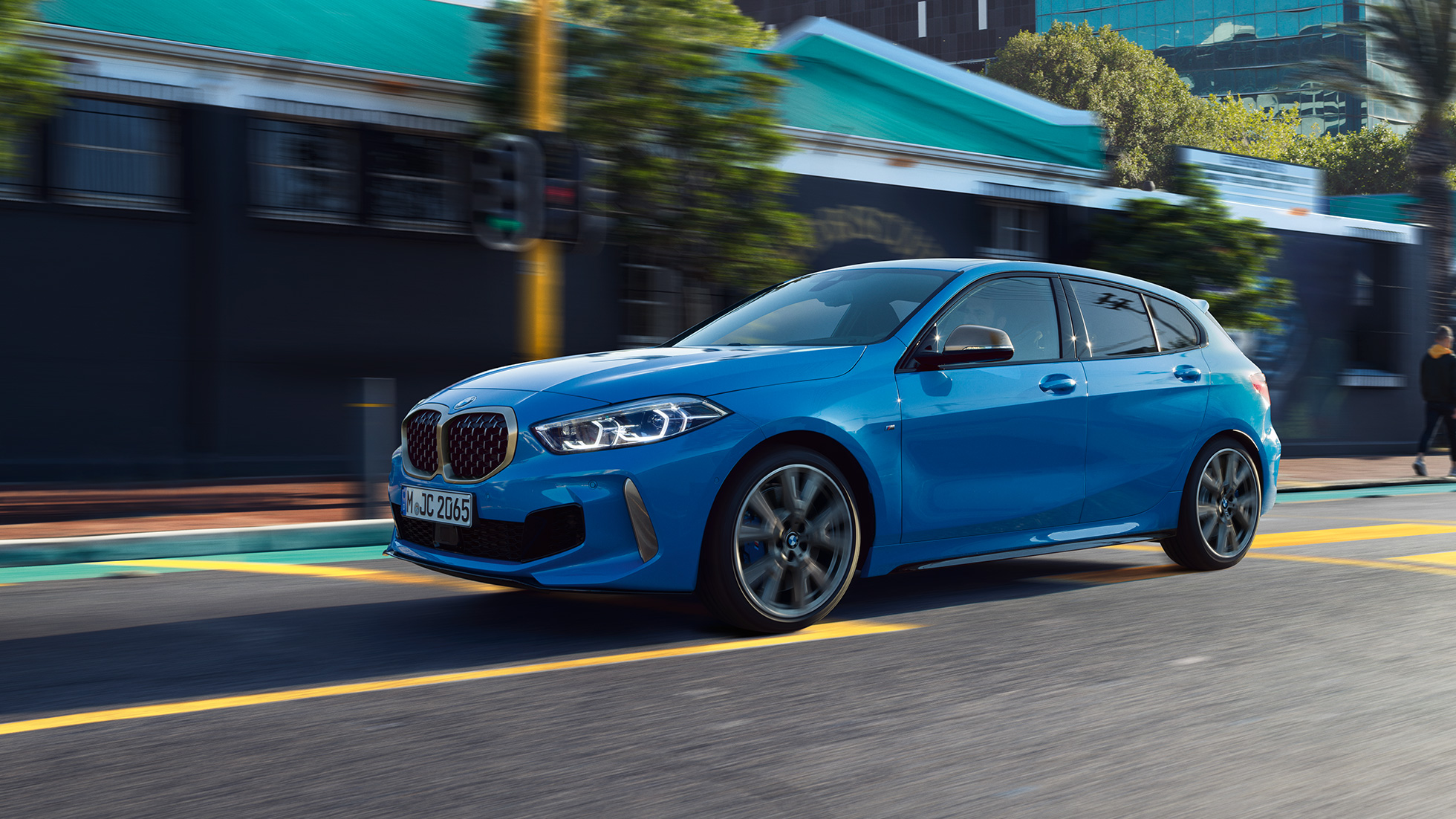 BMW 1. sērija, trīs ceturtdaļu skats no sāna. BMW 1. sērijas metāliskā Misano Blue krāsā, braucošs automobilis no trīs ceturtdaļu skatā no priekšpuses.