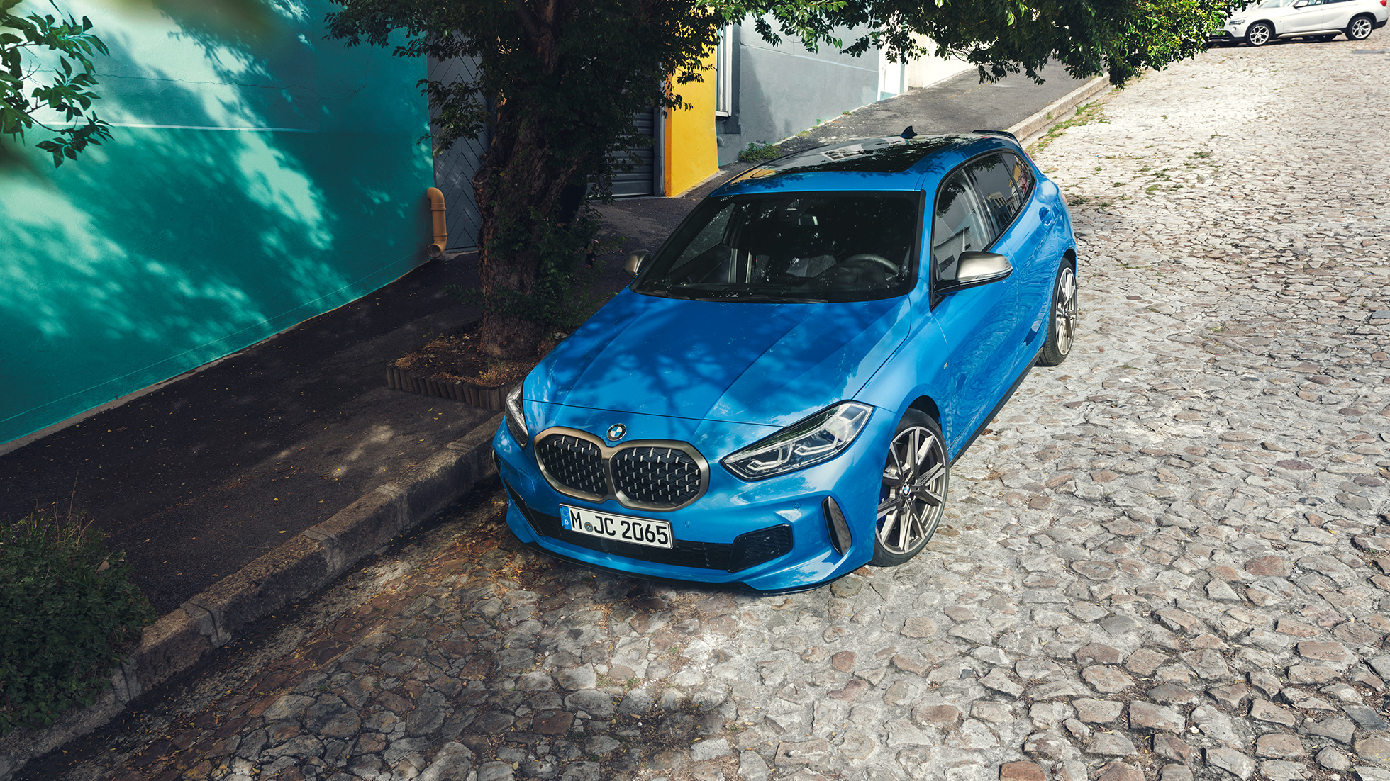 1. sērijas BMW ceļa malā. 1. sērijas BMW metāliskā Misano Blue krāsā, trīs ceturtdaļu skatā no priekšpuses, novietots stāvēšanai ceļa malā skatā no putna lidojuma.