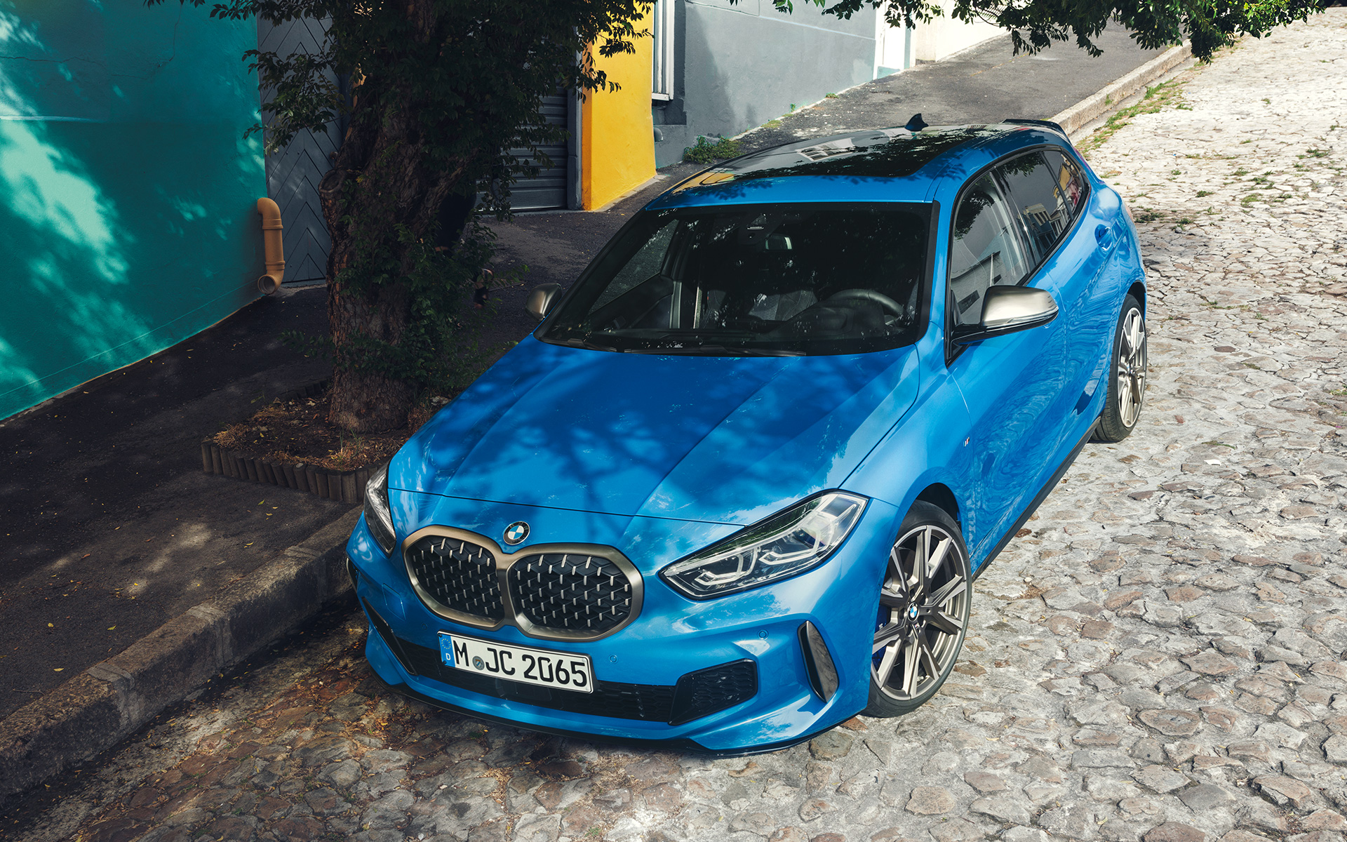 BMW 1. sērijas M135i F40 ceļa malā BMW 1. sērijas M135i F40 metāliskā Misano Blue krāsā, trīs ceturtdaļu skatā no priekšpuses, novietots stāvēšanai ceļa malā skatā no putna lidojuma.