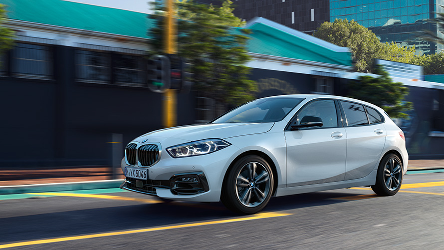 BMW 1. sērija (F40), trīs ceturtdaļu sānskats, braucienā, uz pilsētas ainavas fona BMW 1. sērija (F40), trīs ceturtdaļu sānskats, braucienā, uz pilsētas ainavas fona