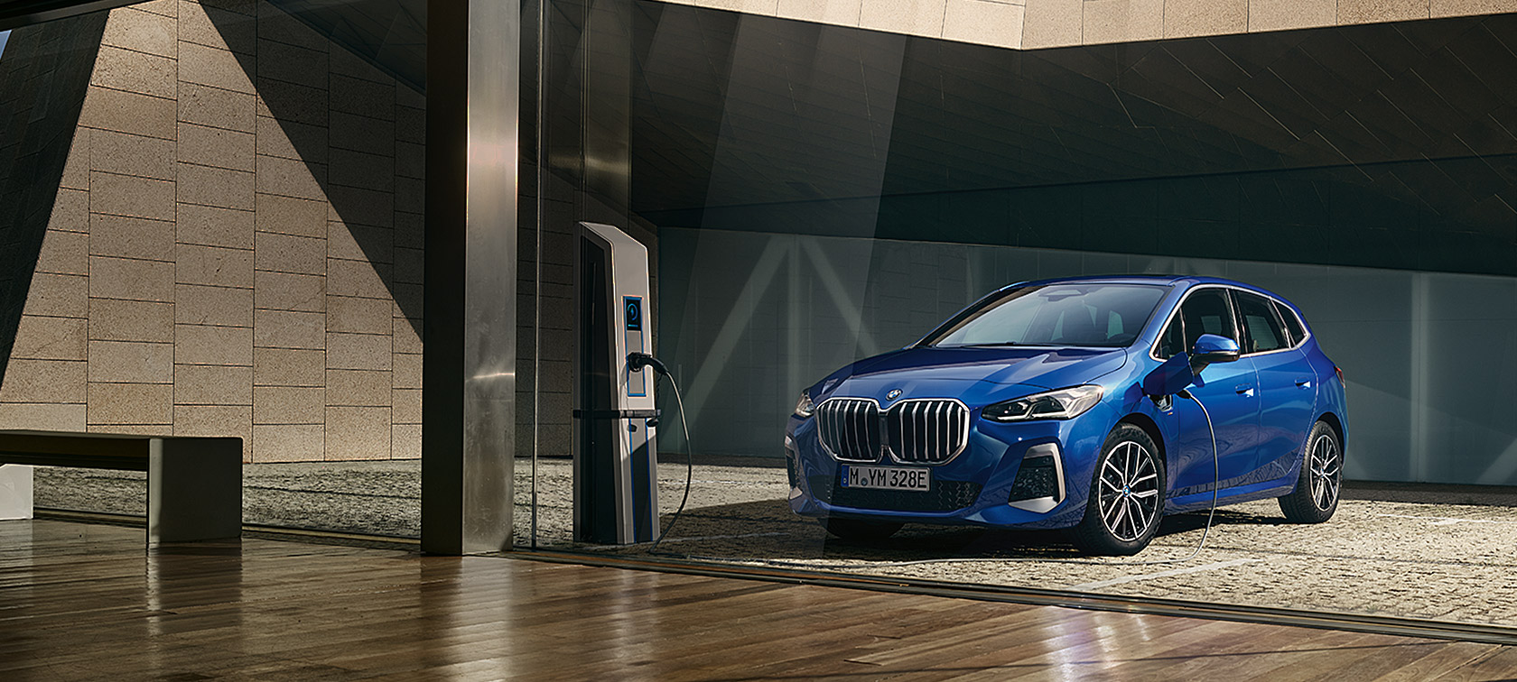 BMW 2. sērijas Active Tourer, 230e, hibrīdauto, U06, 2021, metāliska M Portimao Blue krāsa, trīs ceturtdaļu priekšpuses skats, uzlādes stacijā