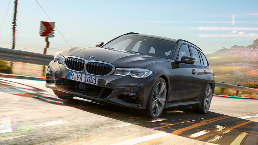 BMW 3. sērijas Touring (G21), Dravit Grey krāsa, trīs ceturtdaļu priekšpuses skats BMW 3. sērijas Touring (G21), Dravit Grey krāsa, trīs ceturtdaļu skats no priekšpuses uz braucošu automobili, šķērsojot tiltu, ar lauku apvidu fonā