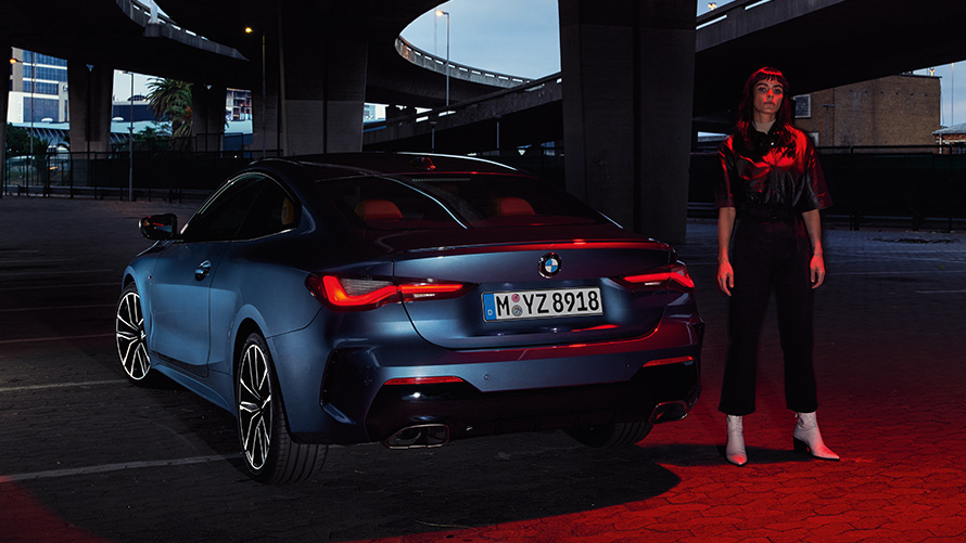 BMW 4. sērijas Coupé (G22), metāliska Arctic Race Blue krāsa, aizmugures skats ar cilvēku BMW 4. sērijas Coupé (G22), metāliska Arctic Race Blue krāsa, aizmugures skats ar cilvēku