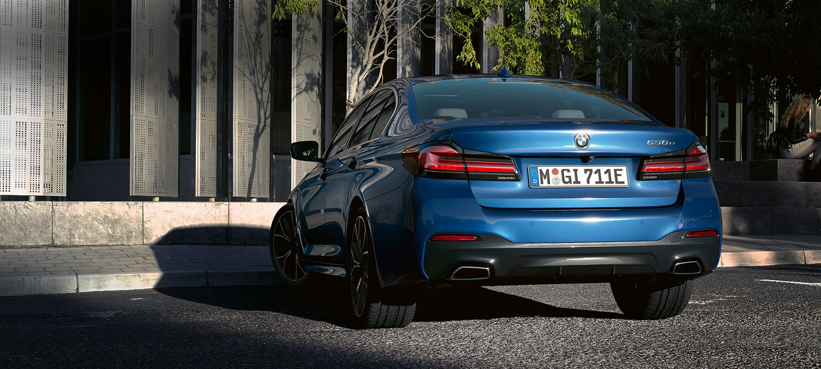 BMW 5. sērijas Sedan eDrive (G30), metāliska Portimao Blue krāsa BMW 5. sērijas Sedan eDrive (G30), metāliska Phytonic Blue krāsa, aizmugures skats, novietots automobilis uz ēkas fona