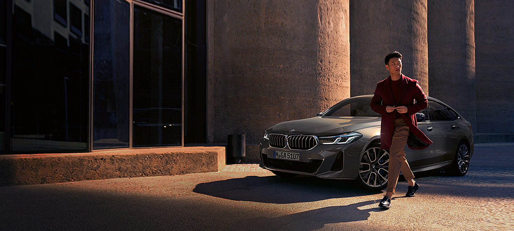 BMW 6. sērijas Gran Turismo 640i xDrive, G32, 2020, Bernina Grey krāsā, vīrietis uz BMW fona, trīs ceturtdaļu priekšpuses skats, stāvošs automobilis