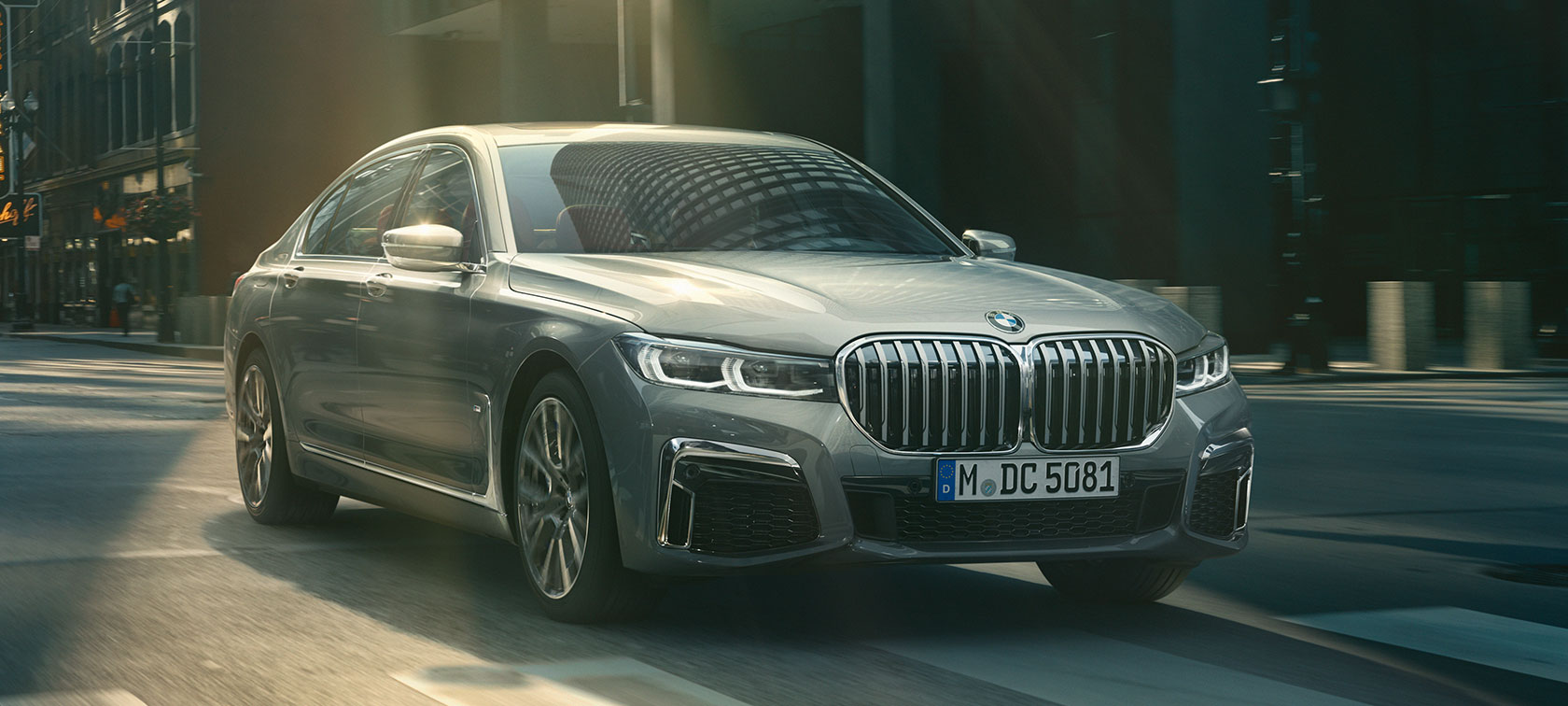 Pelēks BMW 7. sērijas Sedan, braucošs, trīs ceturtdaļu skats no priekšpuses Pelēks BMW 7. sērijas Sedan brauc pa pilsētu trīs ceturtdaļu skatā no priekšpuses