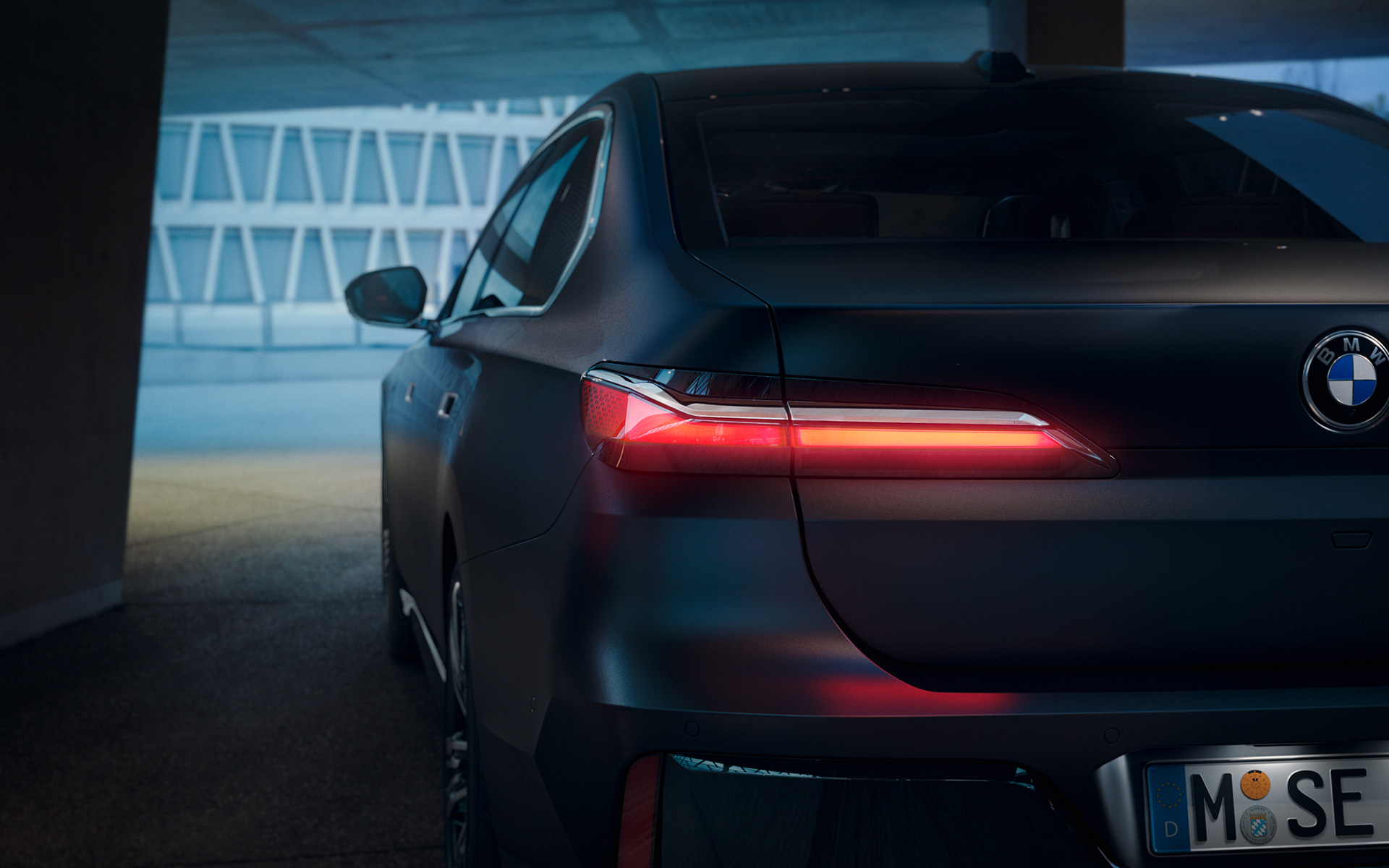 BMW 7. sērijas Sedan, G70, ICE, 740i, M sporta pakotne, metāliska Frozen Deep Grey krāsa, aizmugures skats ar sarkanām spīdošām aizmugurējām gaismām tunelī