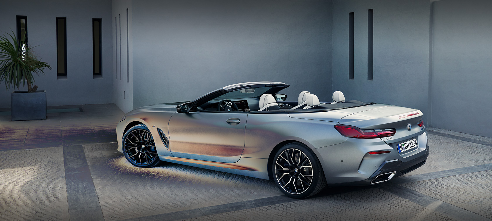 Vīrietis atbalstās pret BMW 8.&nbsp;sērijas Cabrio G14, LCI, atjaunināts, 2022, BMW Individual metāliska Frozen Pure Grey krāsa, sānskats, stāvo&scaron;s automobilis uz ēkas fona ar modeli vīrieti