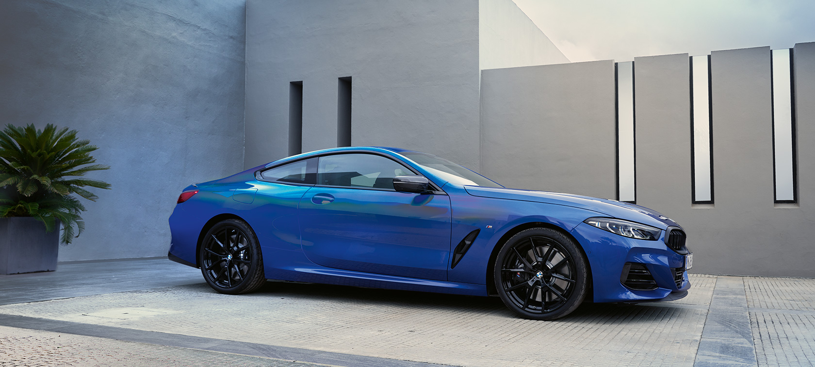 BMW 8. sērijas Coupé G15, LCI, atjaunināts, 2022, metāliska M Portimao Blue krāsa, sānskats, stāvošs automobilis uz ēkas sienas fona