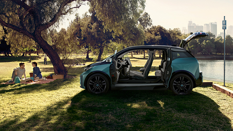 BMW i3 2018 parkā BMW i3 I01 2018, Jucaro Beige krāsa ar metālisku Frozen Grey akcentu, sānskats ar atvērtām durvīm parkā