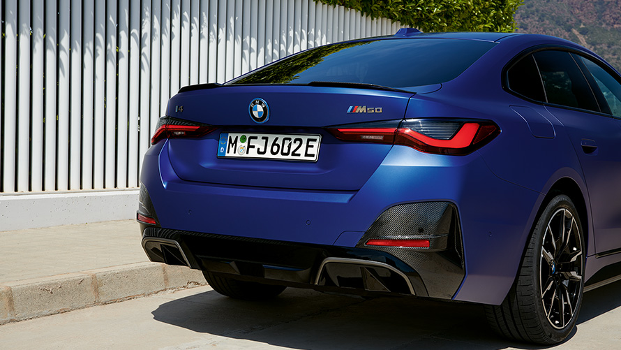 BMW i4 M50, G26, 2021, BMW Individual metāliska Frozen Portimao Blue krāsa, trīs ceturtdaļu aizmugures skats, stāvošs automobilis pie balta žoga