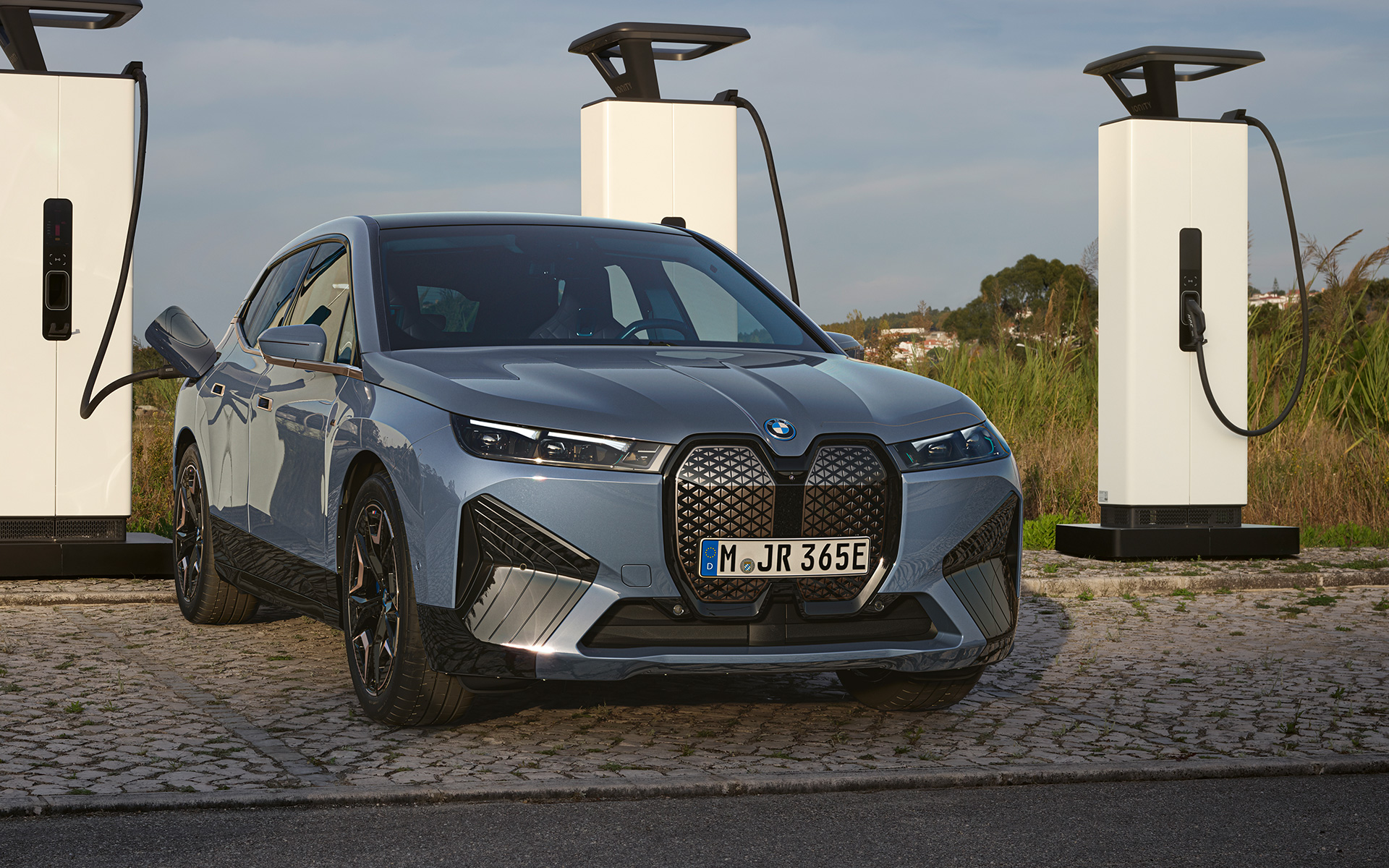 BMW iX M60 i20, 2022, elektrisks SUV, BMW Individual metāliska Storm Bay krāsa, priekšpuses skats, pie lieljaudas uzlādes stacijas
