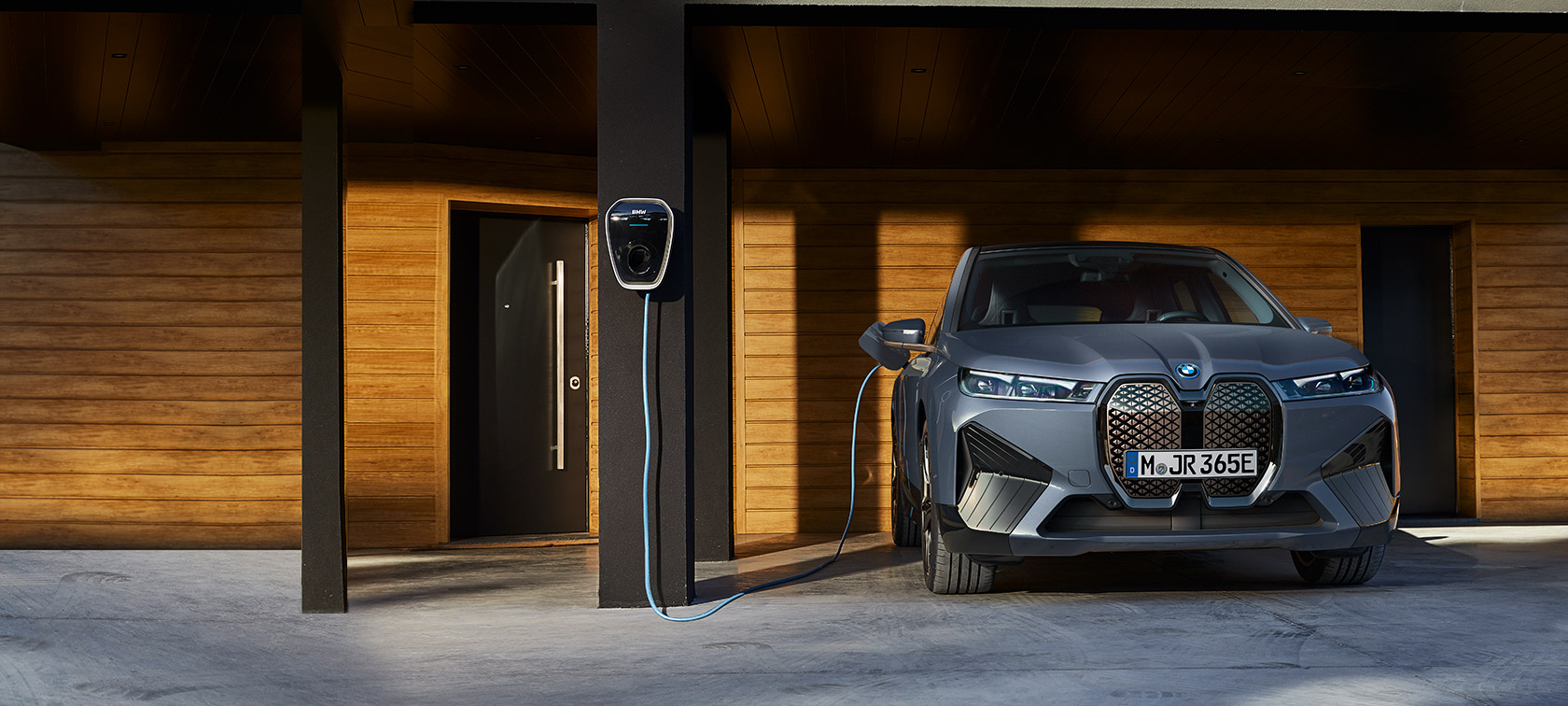 BMW iX M60 i20, 2022, elektrisks SUV, BMW Individual metāliska Storm Bay krāsa, priekšpuses skats, uzlādes laikā pie mājas ar BMW Wallbox