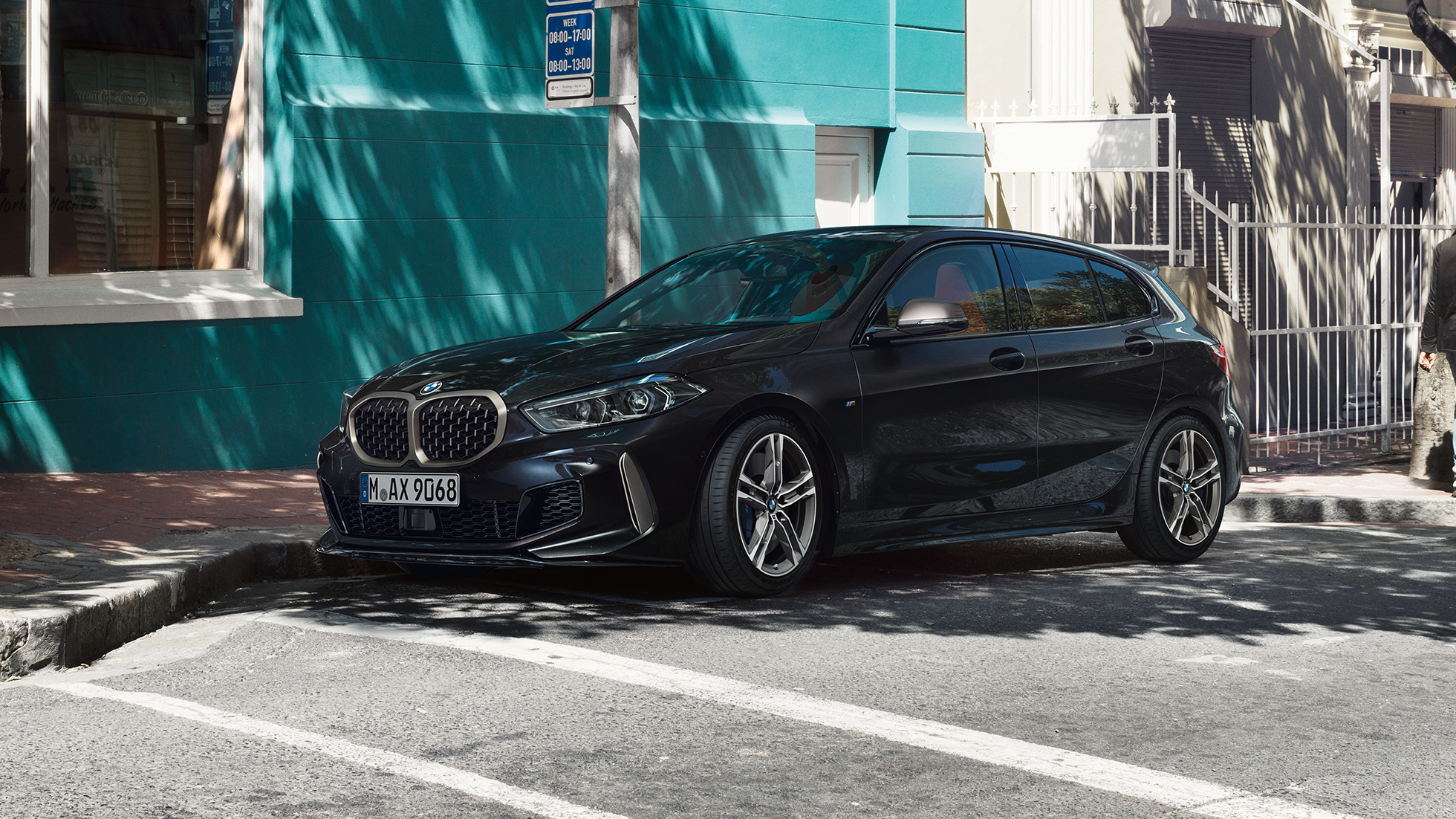 BMW M135i xDrive, trīs ceturtdaļu skats no sāniem. Pilnīgi jaunais BMW M135i xDrive metāliskā Black Sapphire krāsā, trīs ceturtdaļu skata no sāna uz novietotu automobili.