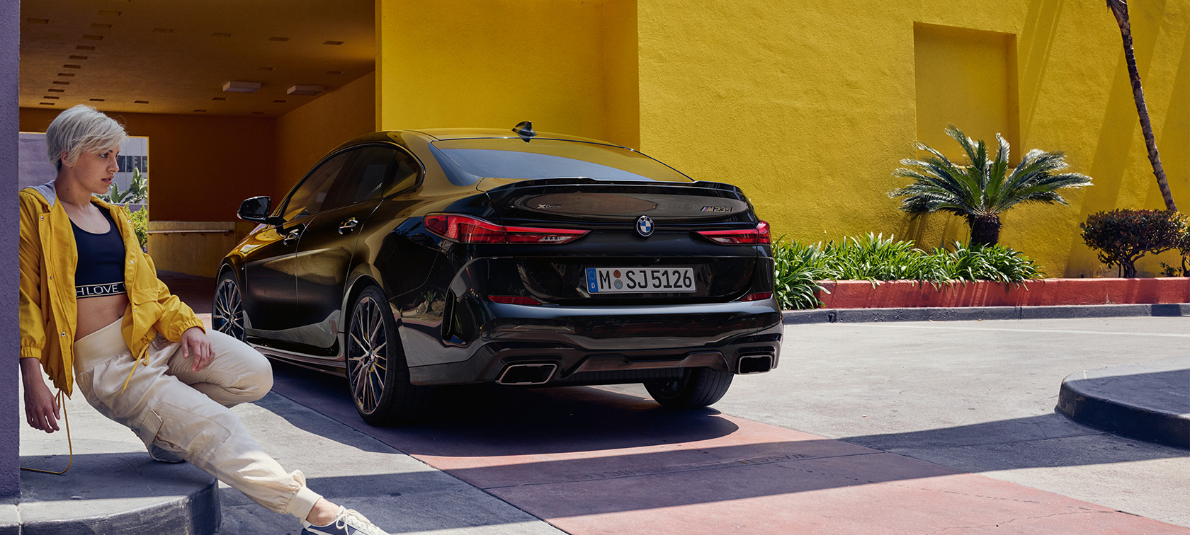 BMW M235i xDrive Gran Coupé, trīs ceturtdaļu aizmugures skats BMW M235i xDrive Gran Coupé, metāliska Black Sapphire krāsa, F44, trīs ceturtdaļu aizmugures skats ar sievieti priekšpusē