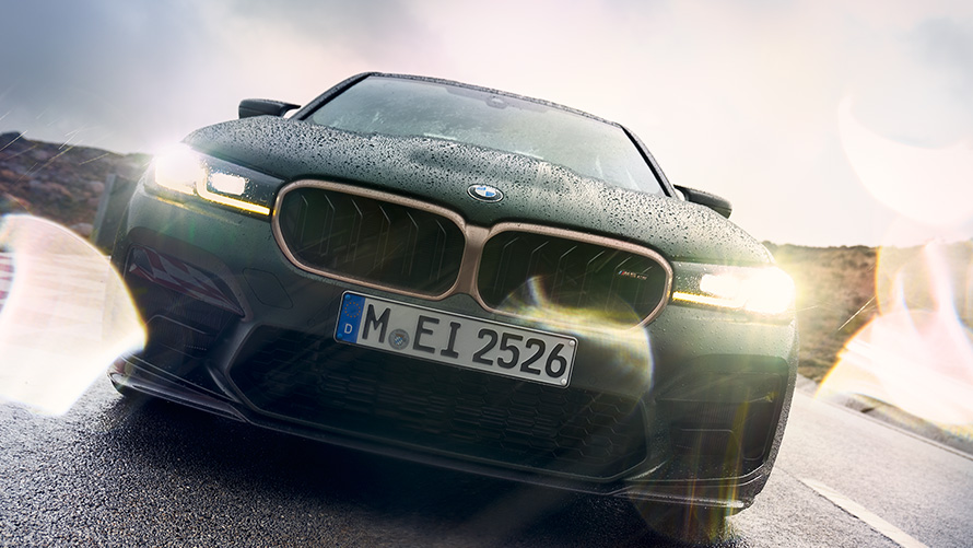 BMW M5 CS, F90, 2021, metāliska Frozen Deep Green krāsa, priekšpuses skats ar ieslēgtiem priekšējiem lukturiem