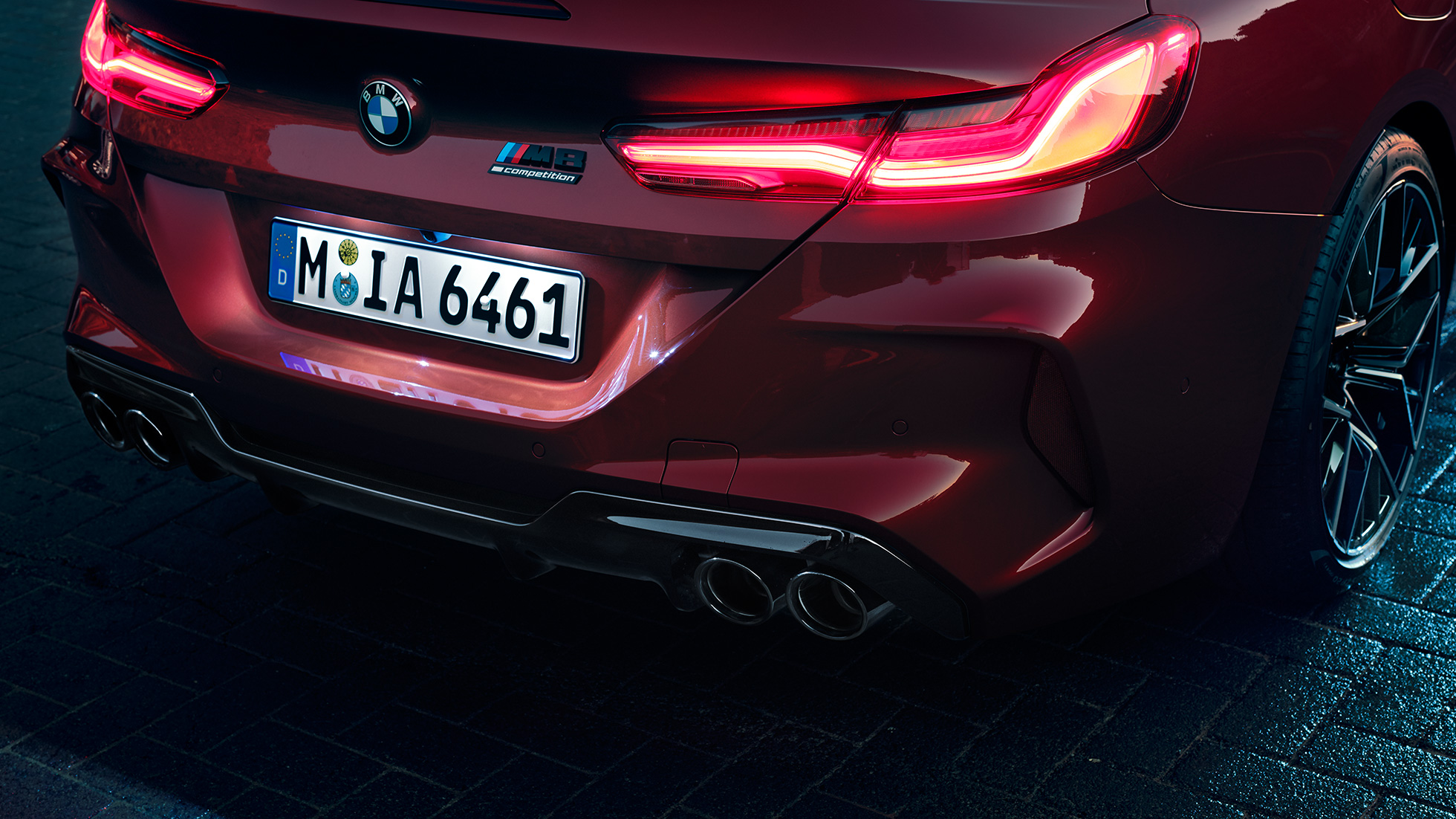 BMW M8 Competition Cabrio, aizmugures tuvplāns. BMW M8 Competition Cabrio metāliskā Motegi Red krāsā, aizmugures tuvplāns ar LED aizmugures lukturiem un M8 Competiton emblēmu.