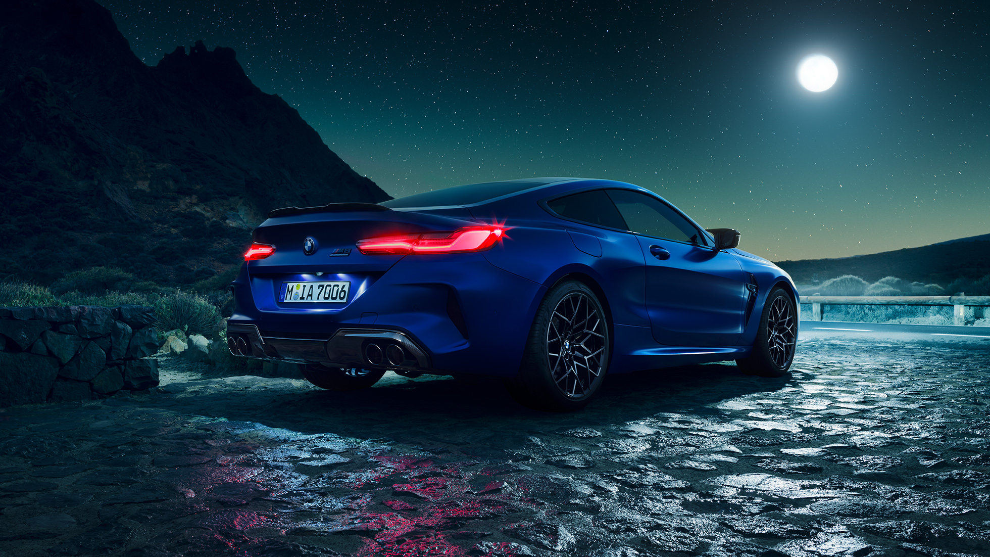 BMW M8 M Competition Coupé, trīs ceturtdaļu skats no aizmugures. BMW M8 Competition Coupé metāliskā Marina Bay Blue krāsā ar iedegtiem LED aizmugurējiem lukturiem, trīs ceturtdaļu skatā no aizmugures ar pilnmēnesi.