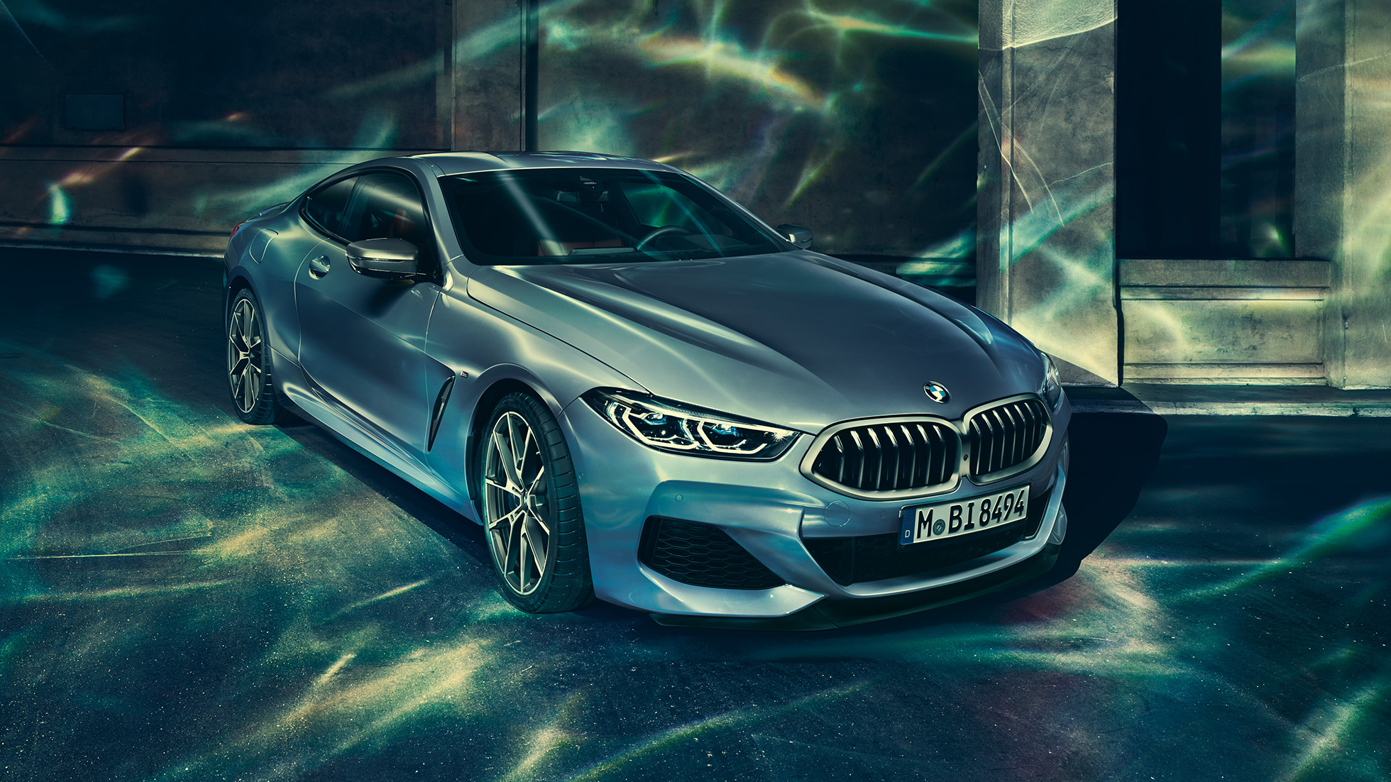 BMW M850i xDrive Coupé, priekšpuse trīs ceturtdaļu skatā no kreisās puses. BMW M850i xDrive metāliskā Barcelona Blue krāsā, trīs ceturtdaļu skats uz stāvēšanai novietotu automobili no priekšpuses uz ēkas fona.