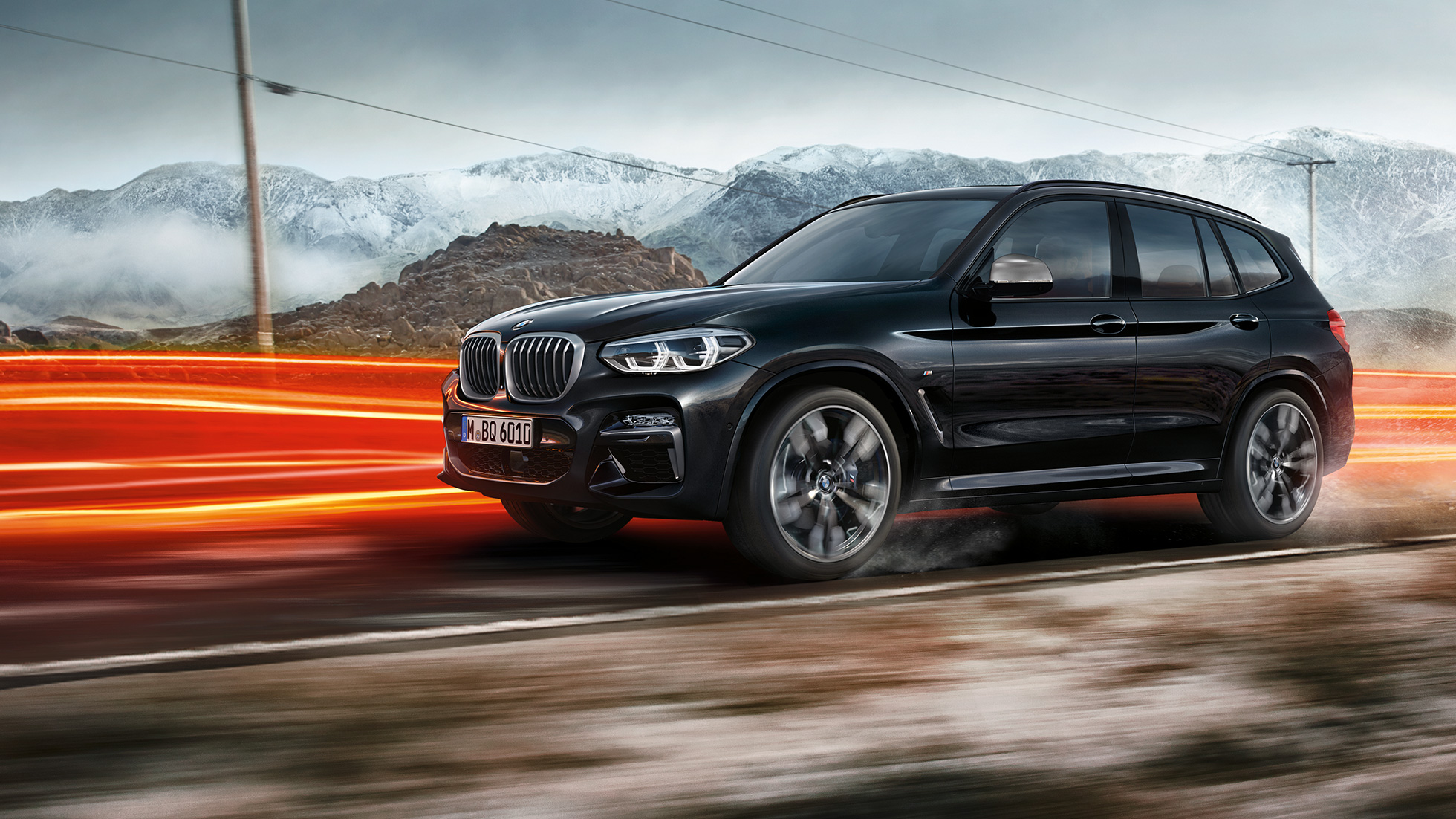 BMW X3 M40i un BMW X3 M40d, skats no sāna. BMW X3 M40i un BMW X3 M40d metāliskā Black Sapphire krāsā, braucošs, virsbūve, skats no sāniem uz kalnu ainavas fona ar gaismas joslām.
