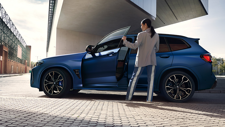 BMW X3 M Competition, F97, LCI, 2021, sānskats, ar atvērtā durvīm un sievieti modeli BMW X3 M Competition, F97, LCI, atjaunināts, 2021, metāliska Frozen Marina Bay Blue krāsa, sānskats, ar atvērtām durvīm un sievieti modeli