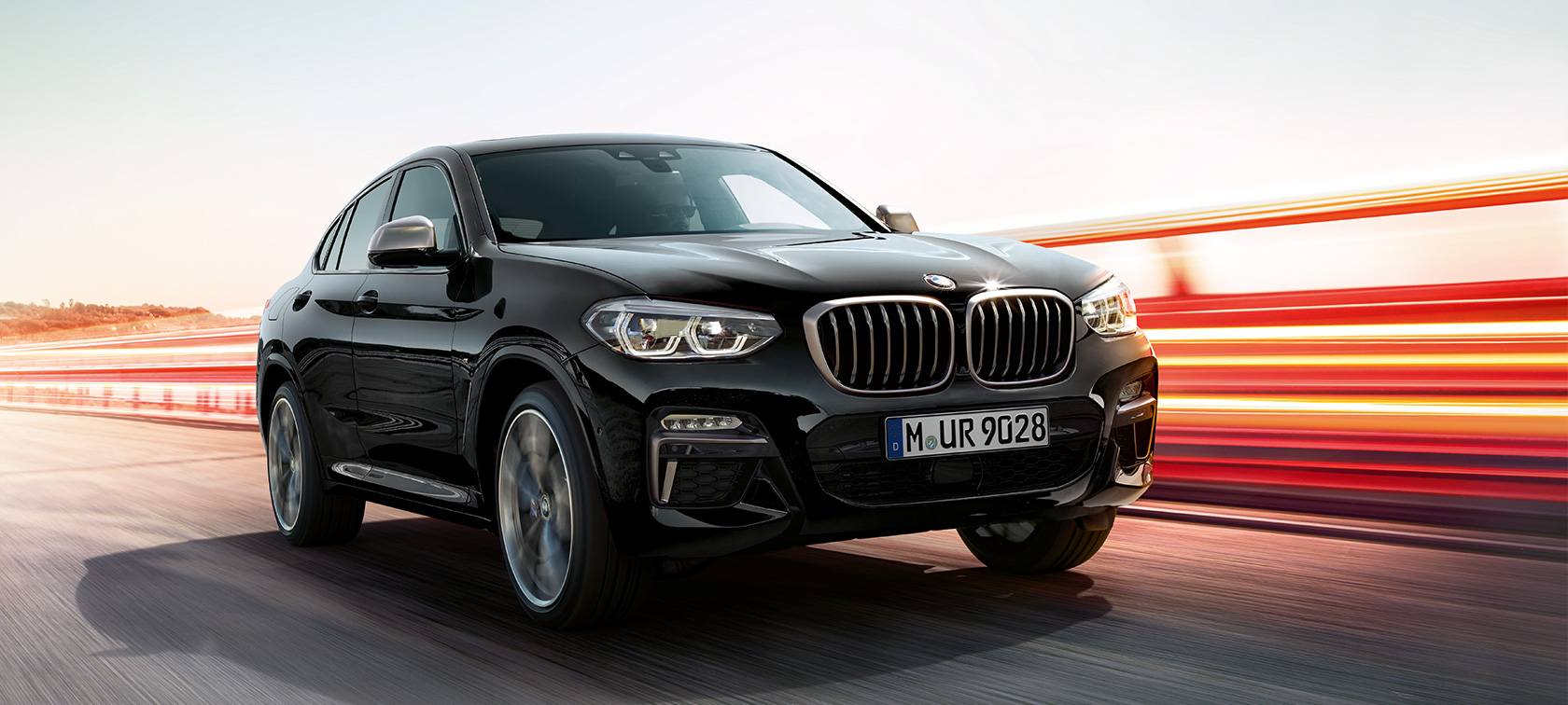 BMW X4 M40i un BMW X4 M40d, trīs ceturtdaļu skats no priekšpuses, kreisā puse. BMW X4 M40i un BMW X4 M40d metāliskā Black Sapphire krāsā, virsbūve, trīs ceturtdaļu skats no priekšpuses, kreisais sāns, ar gaismas joslām.