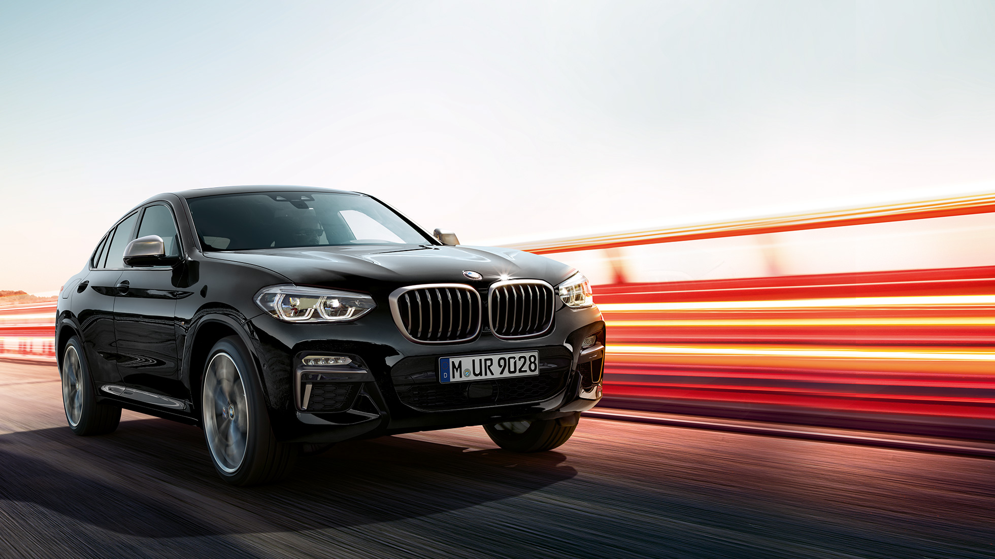 BMW X4 M40i, trīs ceturtdaļu skats no aizmugures. BMW X4 M40i metāliskā Black Sapphire krāsā, braucošs, virsbūve, trīs ceturtdaļu skats no aizmugures ar gaismas joslām.