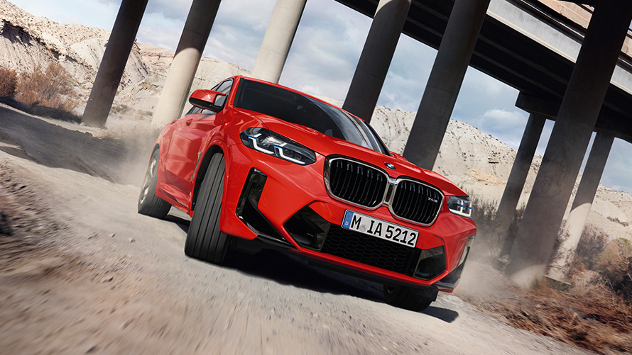 BMW X4 M, F98, LCI, atjaunināts, 2021, metāliska Toronto Red krāsa, trīs ceturtdaļu priekšpuses skats, uz tilta kolonnu fona