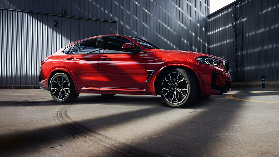 BMW X4 M, F98, LCI, atjaunināts, 2021, metāliska Toronto Red krāsa, sānskats, uz rūpnīcas ēkas fona