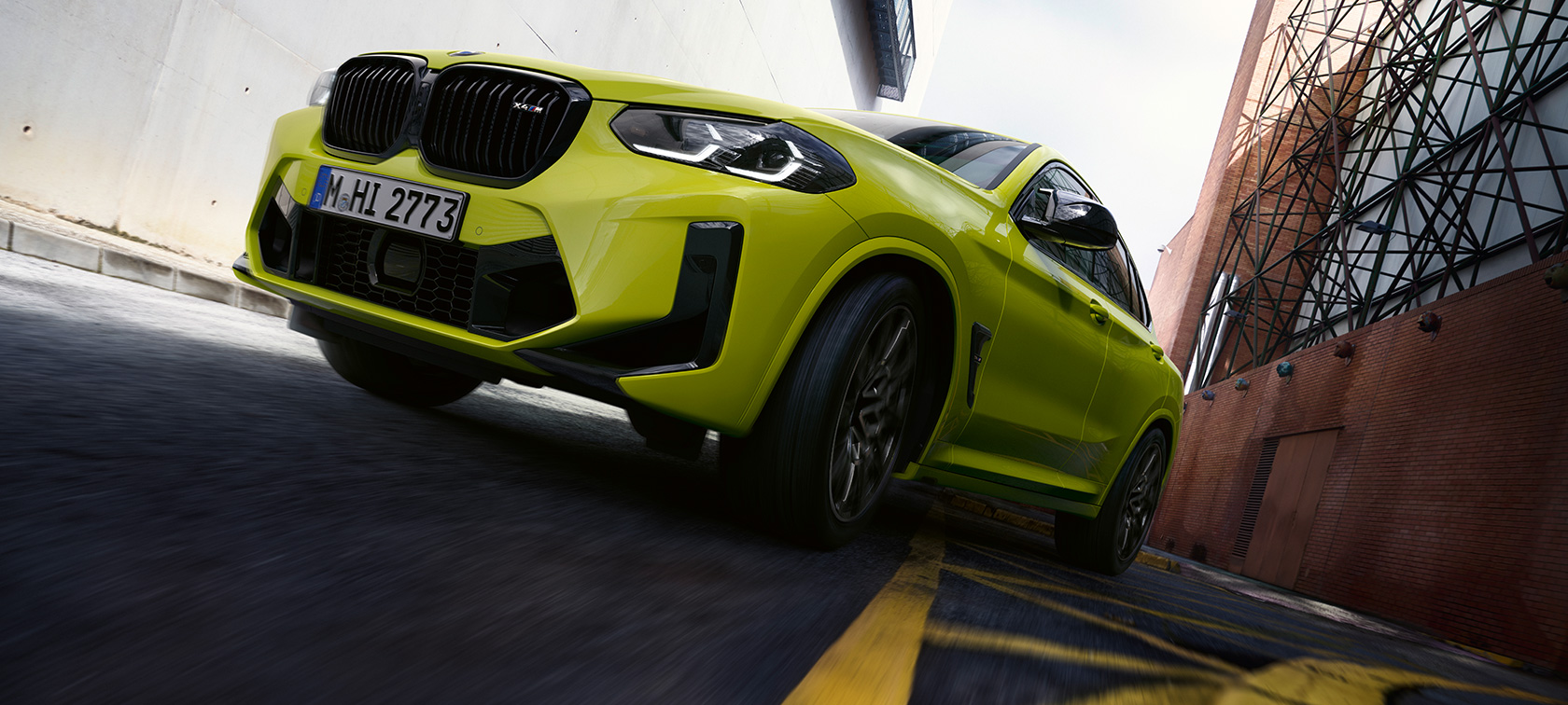 BMW X4 M Competition, F98, LCI, atjaunināts, 2021, Sao Paulo Yellow krāsa, trīs ceturtdaļu priekšpuses skats ar skatu no apakšas, braucienā cauri kanjonam ar mājām