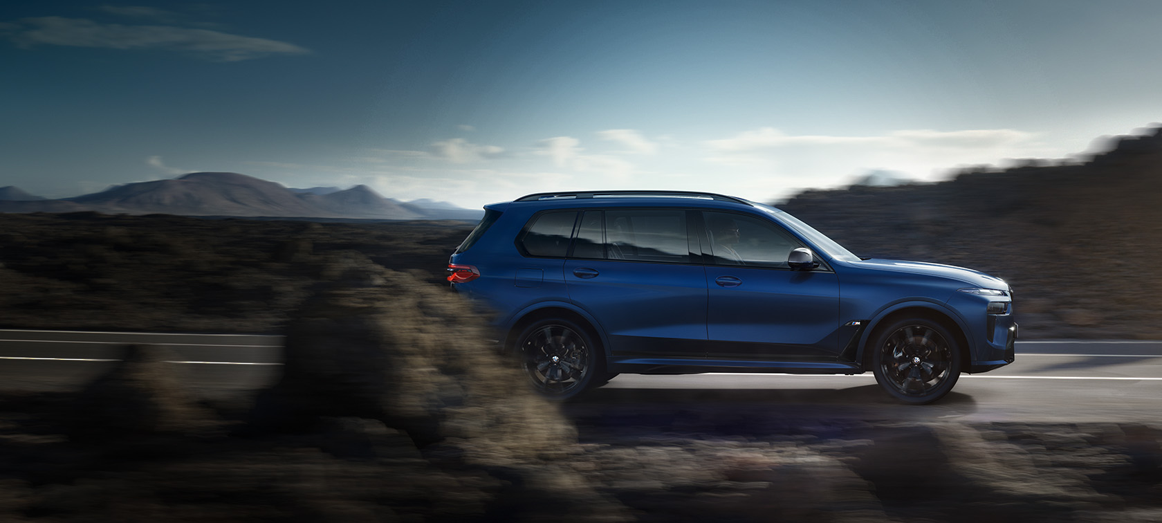 BWM X7 M60i xDrive, G07, LCI, Frozen Marina Bay Blue krāsa, sānskats, braucienā pa ielu BWM X7 M60i xDrive, G07, LCI, Frozen Marina Bay Blue krāsa, sānskats, braucienā pa ielu, uz kalnu ainavas fona