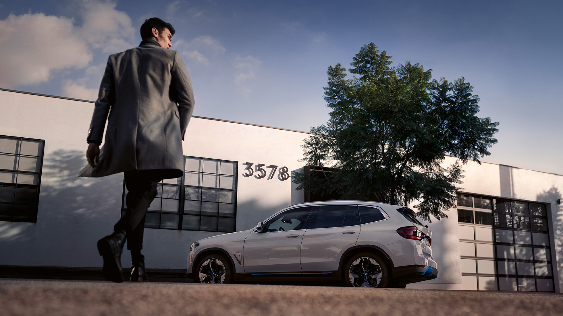 BMW iX3, G08, 2020, sānskats uz ēkas fona ar vīrieti BMW iX3, G08, 2020, metāliska Mineral White krāsa, sānskats uz ēkas fona ar vīrieti