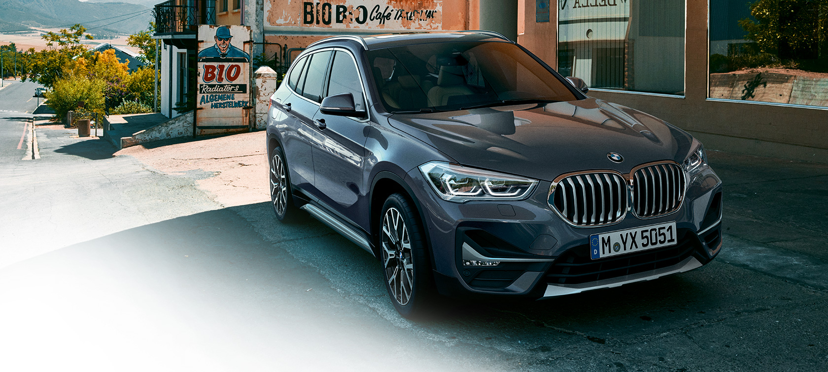 BMW X1, trīs ceturtdaļu skats no priekšpuses. BMW X1, trīs ceturtdaļu skats no priekšpuses uz braucošu automobili uz pilsētas ainavas fona.