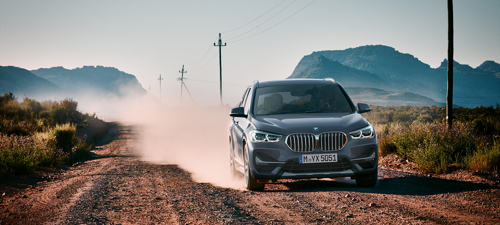 BMW X1, trīs ceturtdaļu skats no aizmugures. BMW X1, trīs ceturtdaļu skats no aizmugures uz braucošu automobili uz kalnu ainavas fona.