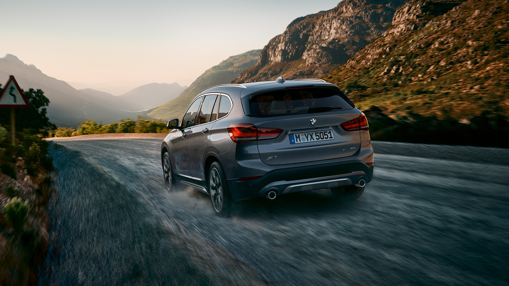 BMW X1, trīs ceturtdaļu skats no aizmugures. BMW X1, trīs ceturtdaļu skats no aizmugures uz braucošu automobili uz kalnu ainavas fona.