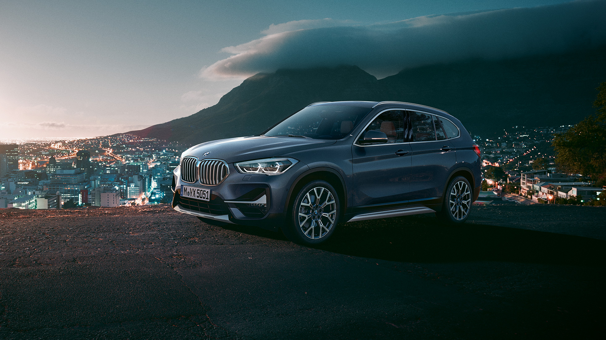 BMW X1, trīs ceturtdaļu skats no sāniem. BMW X1, trīs ceturtdaļu skats no sāniem uz stāvošu automobili uz pilsētas ainavas fona.