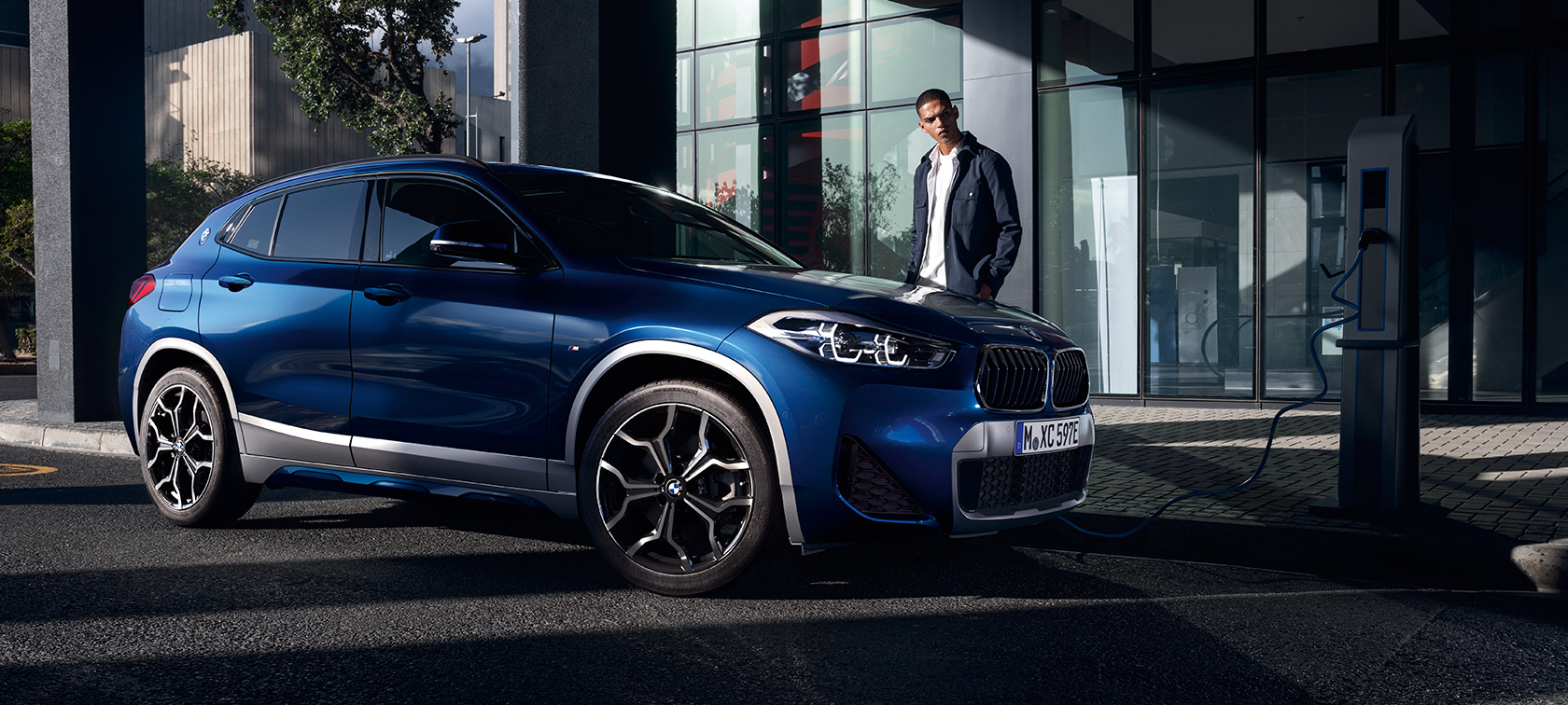Hibrīdauto, BMW X2 xDrive25e, F39, trīs ceturtdaļu sānskats, uzlādes stacijā Hibrīdauto, BMW X2 xDrive25e, F39, trīs ceturtdaļu sānskats, uzlādes stacijā ar modeli
