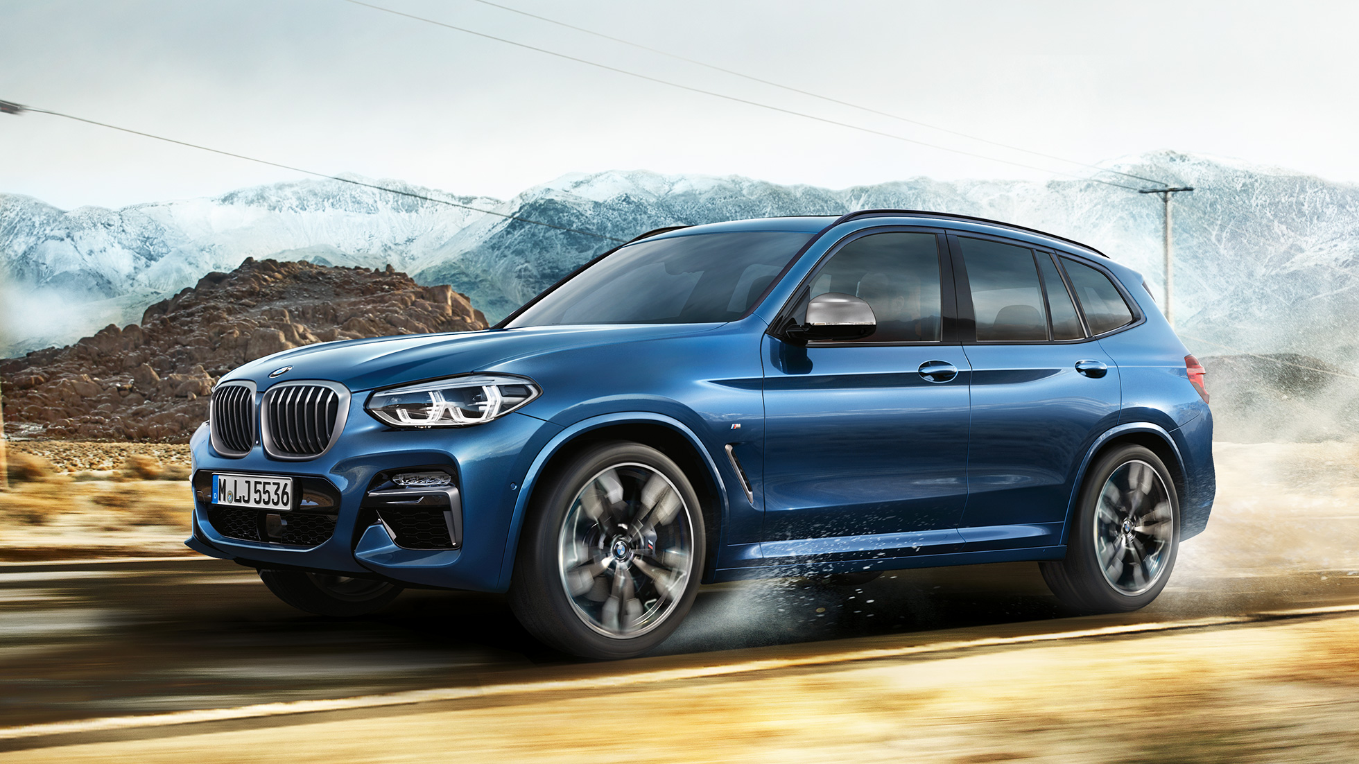 BMW X3 M40i, skats uz vidusdaļu ar disku un priekšējo spārnu uz kalnu fona BMW X3 M40i, skats uz vidusdaļu ar disku un priekšējo spārnu uz kalnu fona