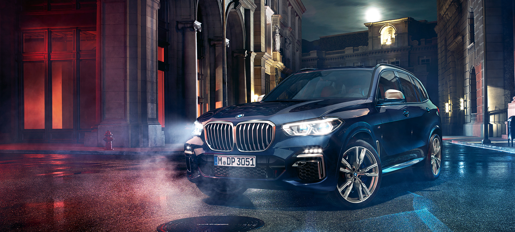 BMW X5 M50d uz ceļa BMW X5 M50d, stāvot uz ceļa ar naksnīgu pilsētu fonā